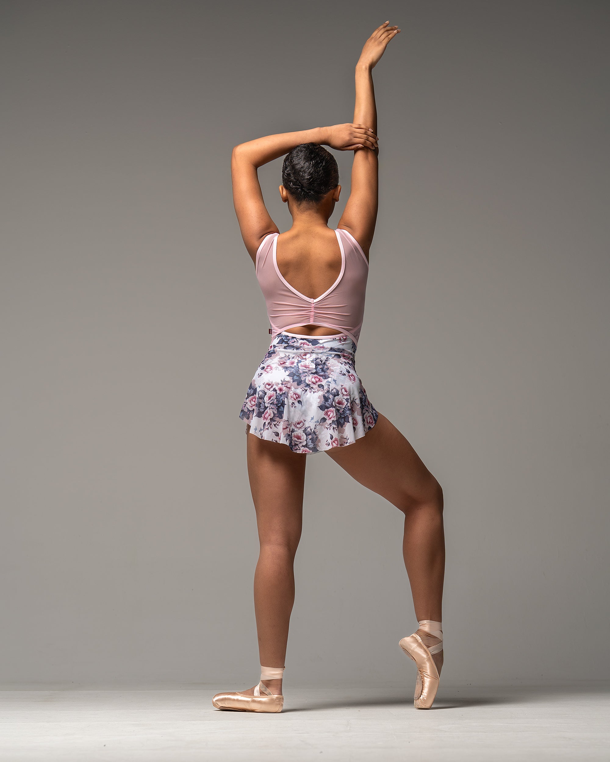 Dancer wearing white pink and blue leotard with matching short ballet skirt. Back view