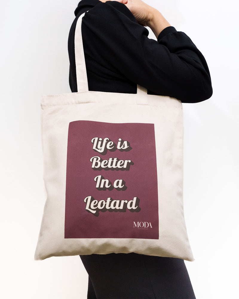 Tote bag with 'Life is Better In a Leotard' text held by a person against a white background. Dance bag.